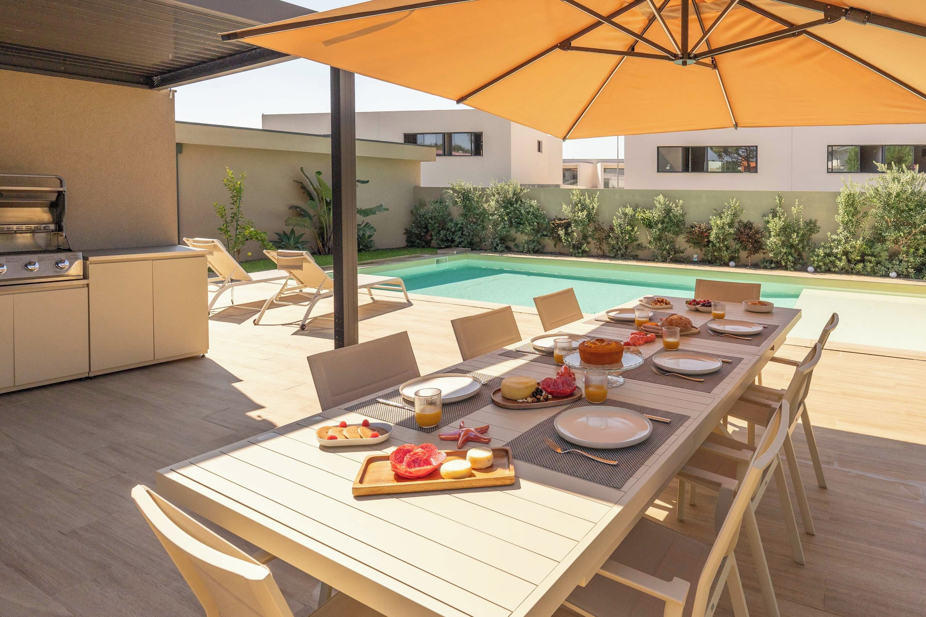 Un área de comedor al aire libre con piscina, una parrilla y una mesa lista para una comida.