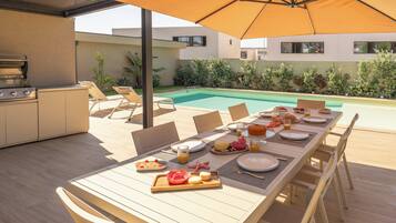 Un área de comedor al aire libre con piscina, una parrilla y una mesa lista para una comida.