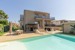 A modern two-story house with a swimming pool, outdoor seating, and a well-maintained garden.