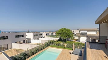 A modern residential area with a swimming pool, a view of the sea, and a tree.