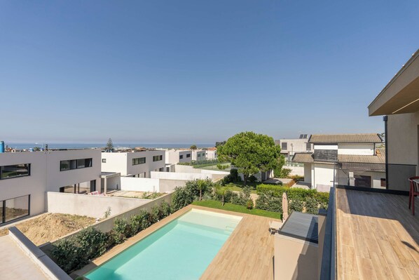 A modern residential area with a swimming pool, a view of the sea, and a tree.