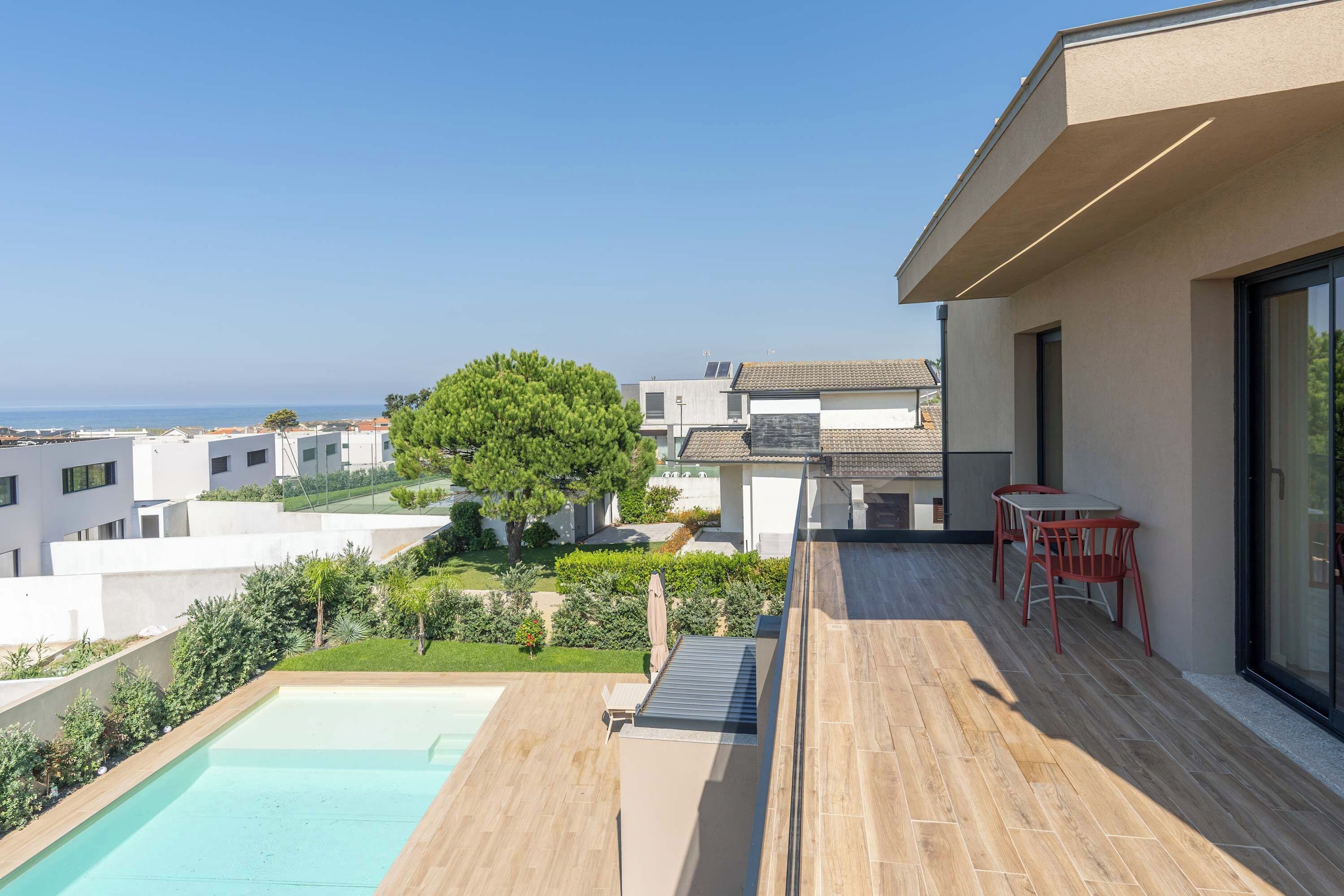 Un moderno edificio residencial con piscina, mobiliario exterior y vista al mar.