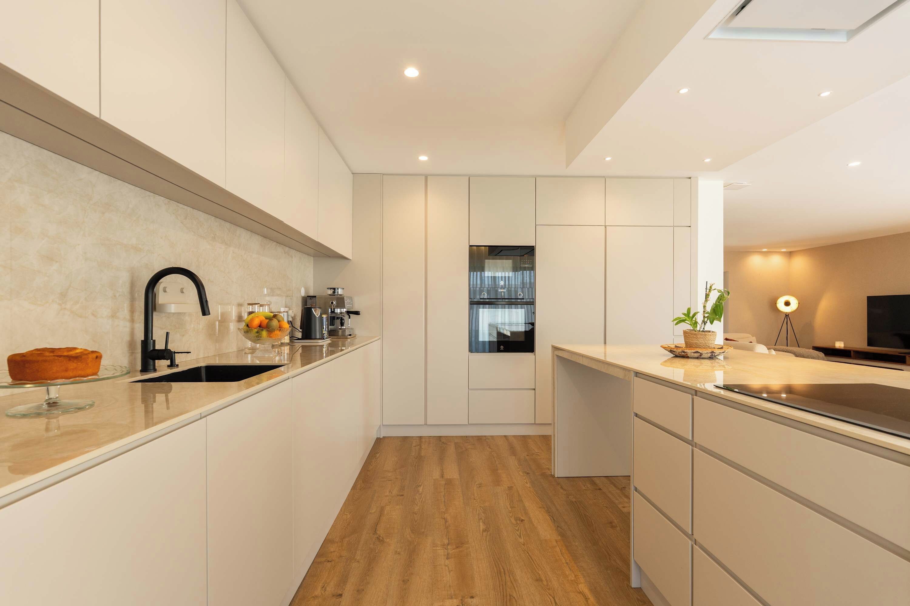 A modern kitchen with a wooden floor, white cabinetry, a built-in oven, and a coffee machine.