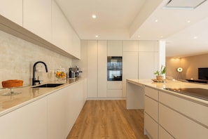 Una cocina moderna con suelo de madera, armarios blancos, horno empotrado y cafetera.