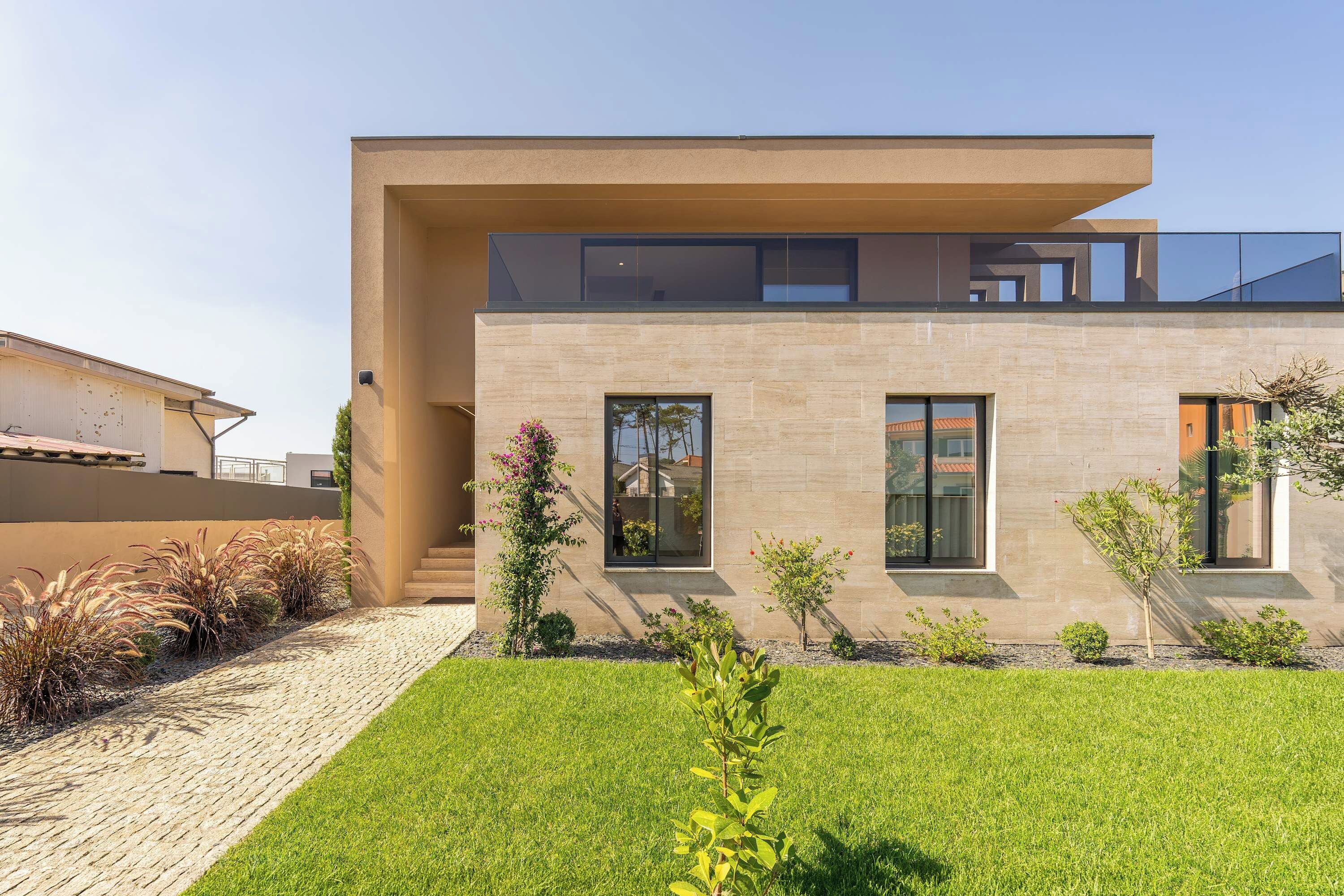 Una casa moderna de dos pisos con techo plano, ventanas grandes y un césped bien cuidado.