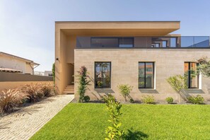 A modern two-story house with a flat roof, large windows, and a well-maintained lawn.