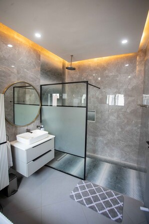 Un bagno moderno con cabina doccia in vetro, un mobile lavabo bianco con specchio tondo e un tappeto decorativo sul pavimento.
