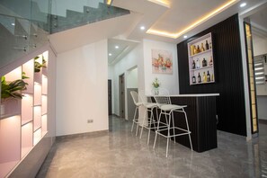 Un interno moderno con una scala in vetro, un'area bar con sedute bianche e una parete con esposizione di liquori.