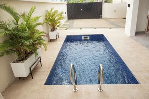 Ein rechteckiger Swimmingpool mit zwei Metallleitern, umgeben von beigen Fliesen und Topfpflanzen.
