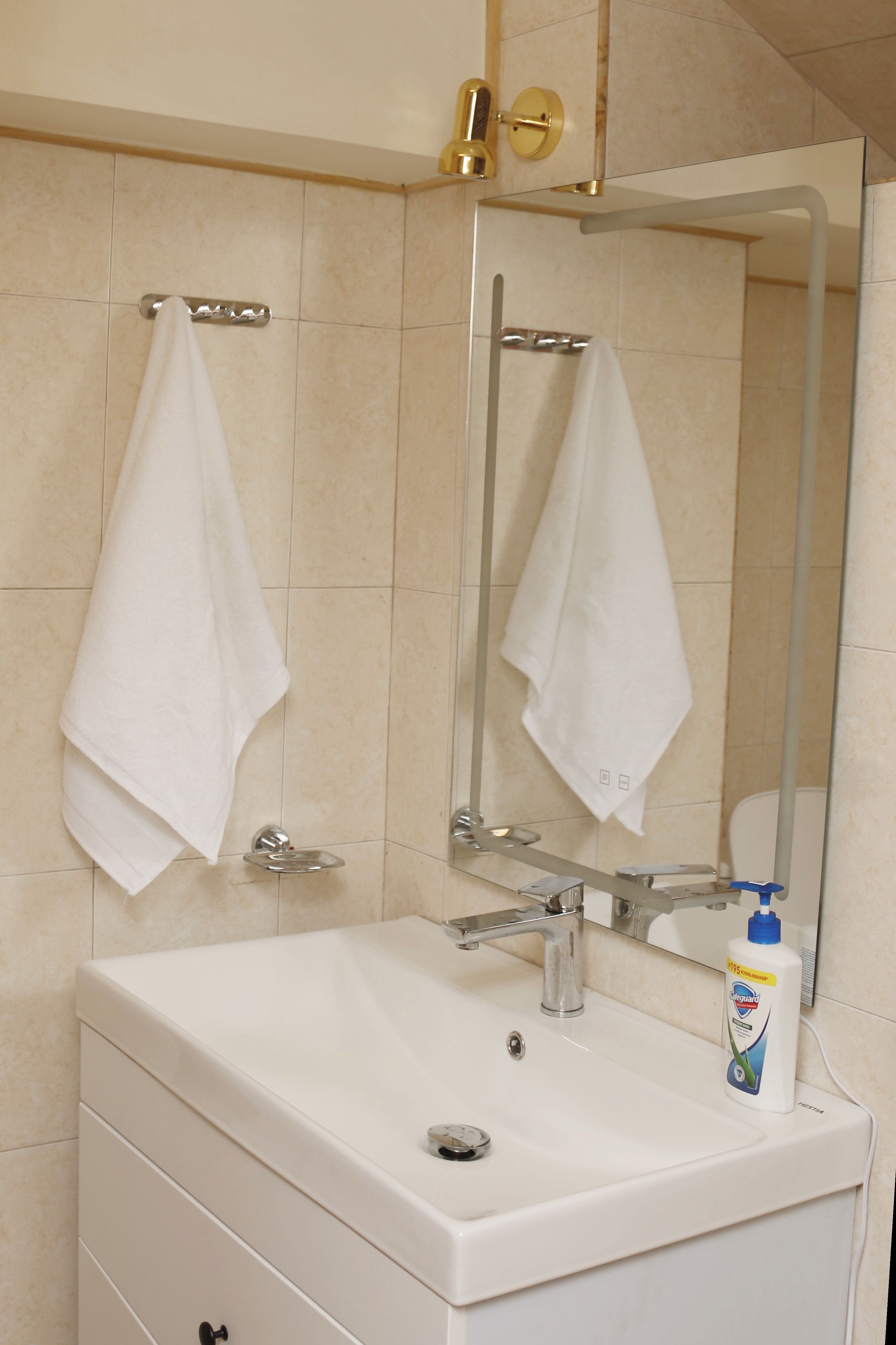 Un baño con un lavamanos blanco, un espejo y dos toallas colgadas en barras para toallas.