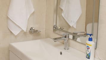 Un baño con un lavamanos blanco, un espejo y dos toallas colgadas en barras para toallas.