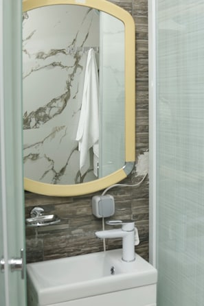 Un baño con pared de mármol, un espejo con marco amarillo, un lavabo blanco y una toalla colgada en la pared.