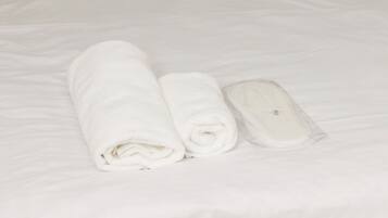 A bed with white linens, two rolled towels, and a wooden headboard.
