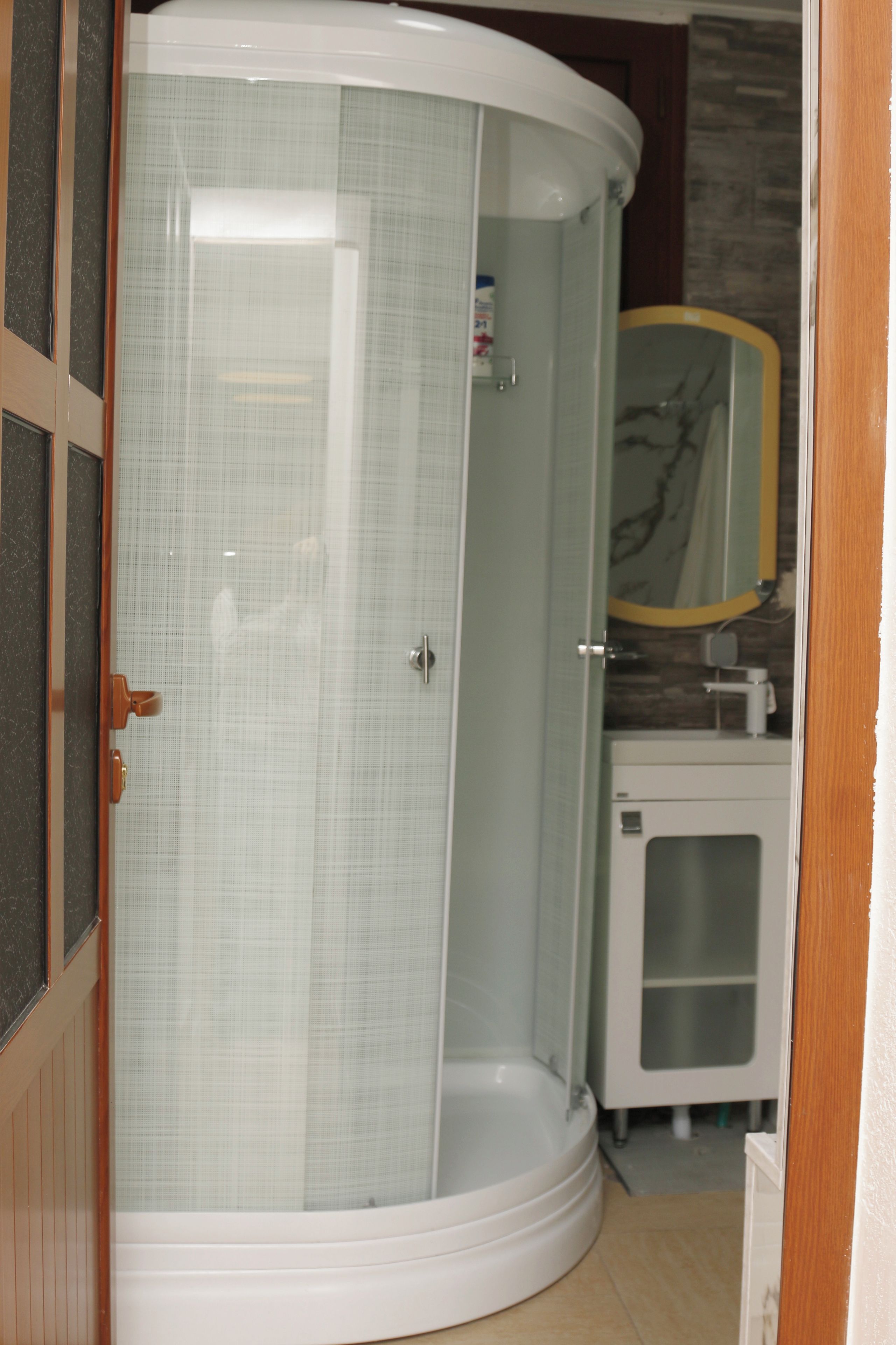 A corner shower enclosure with a glass door, a white sink, and a mirror above it.