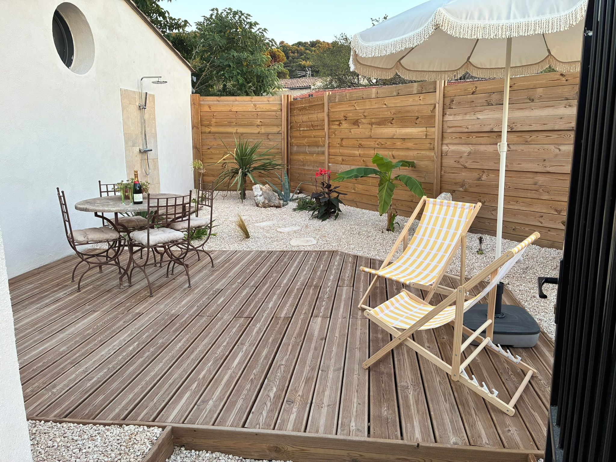 Eine Holzterrasse mit Tisch und Stühlen, umgeben von einem Holzzaun und Kübelpflanzen.