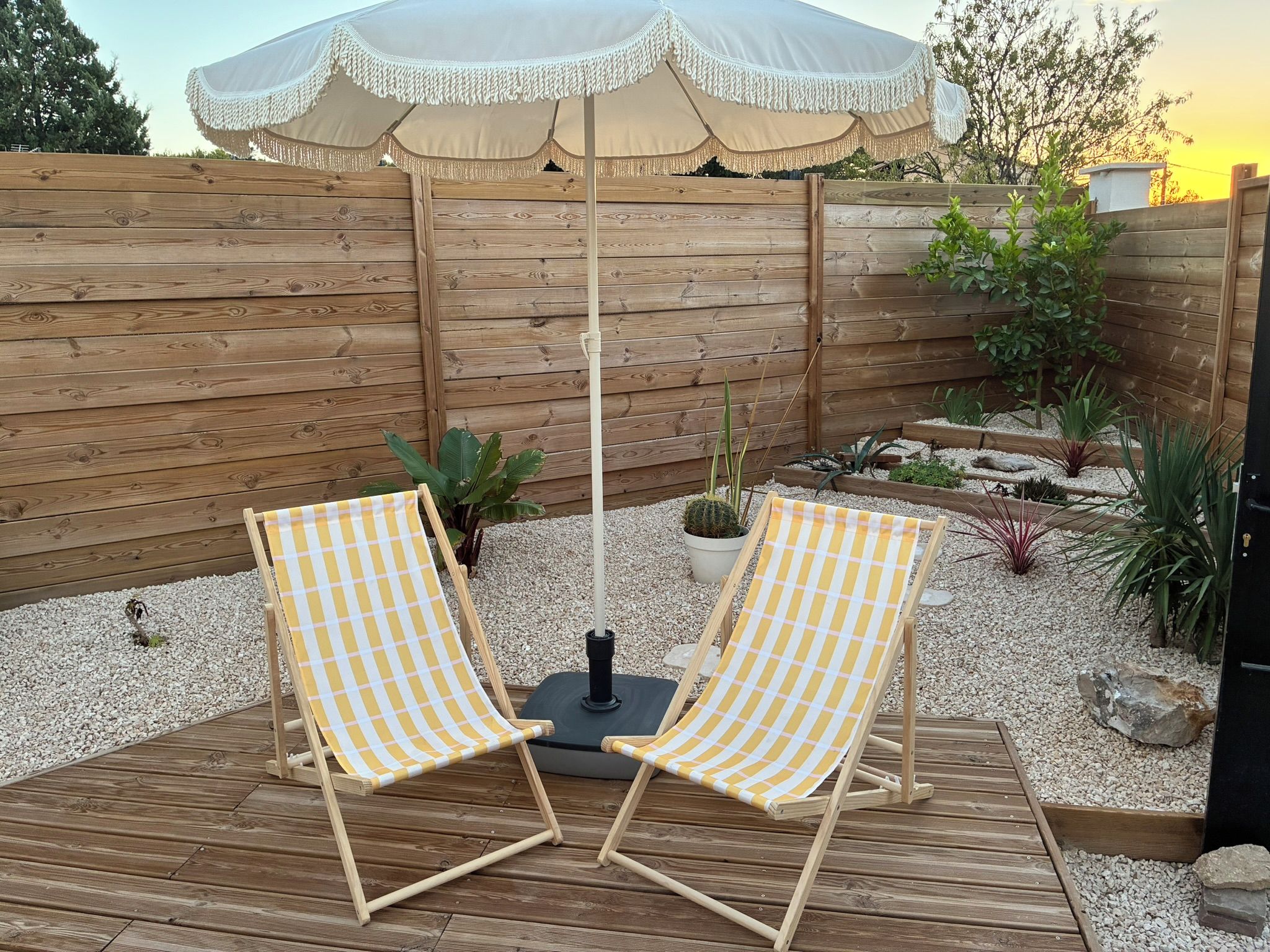 Une terrasse en bois avec deux chaises longues à motifs à carreaux et un parasol blanc.