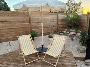 Una terraza de madera con dos sillones a cuadros y una sombrilla blanca.