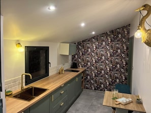 A modern kitchen with a wooden countertop, a sink, a window, and a decorative wall with a floral pattern. - Amoryna (Cavaillon)