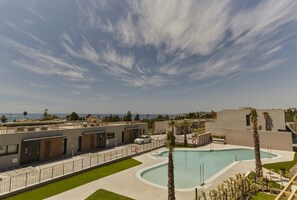 Ein moderner Gebäudekomplex mit Schwimmbad, blauem Himmel und Blick auf den Ozean.