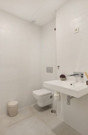 Ein modernes Badezimmer mit Toilette, Waschbecken und Dusche, alles in Weiß.