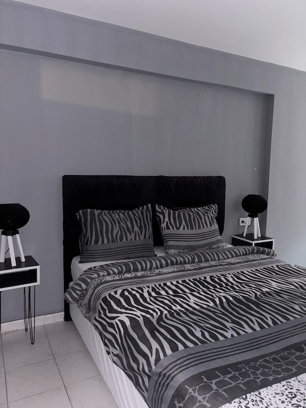 Un dormitorio moderno con una colcha de estampado de cebra, un cabecero negro y dos mesitas de noche con lámparas redondas negras.