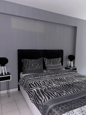 A modern bedroom with a zebra-patterned bedspread, a black headboard, and two bedside tables with round black lamps. - Turkey Home Village 55 (Lübben (Spreewald))