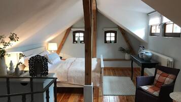 A cozy attic bedroom with a sloped ceiling, a bed, a chair, a table, and a radiator.