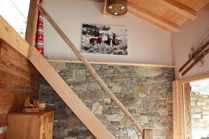 Una habitación con pared de piedra, vigas de madera y un cuadro de ciervos en un paisaje nevado.