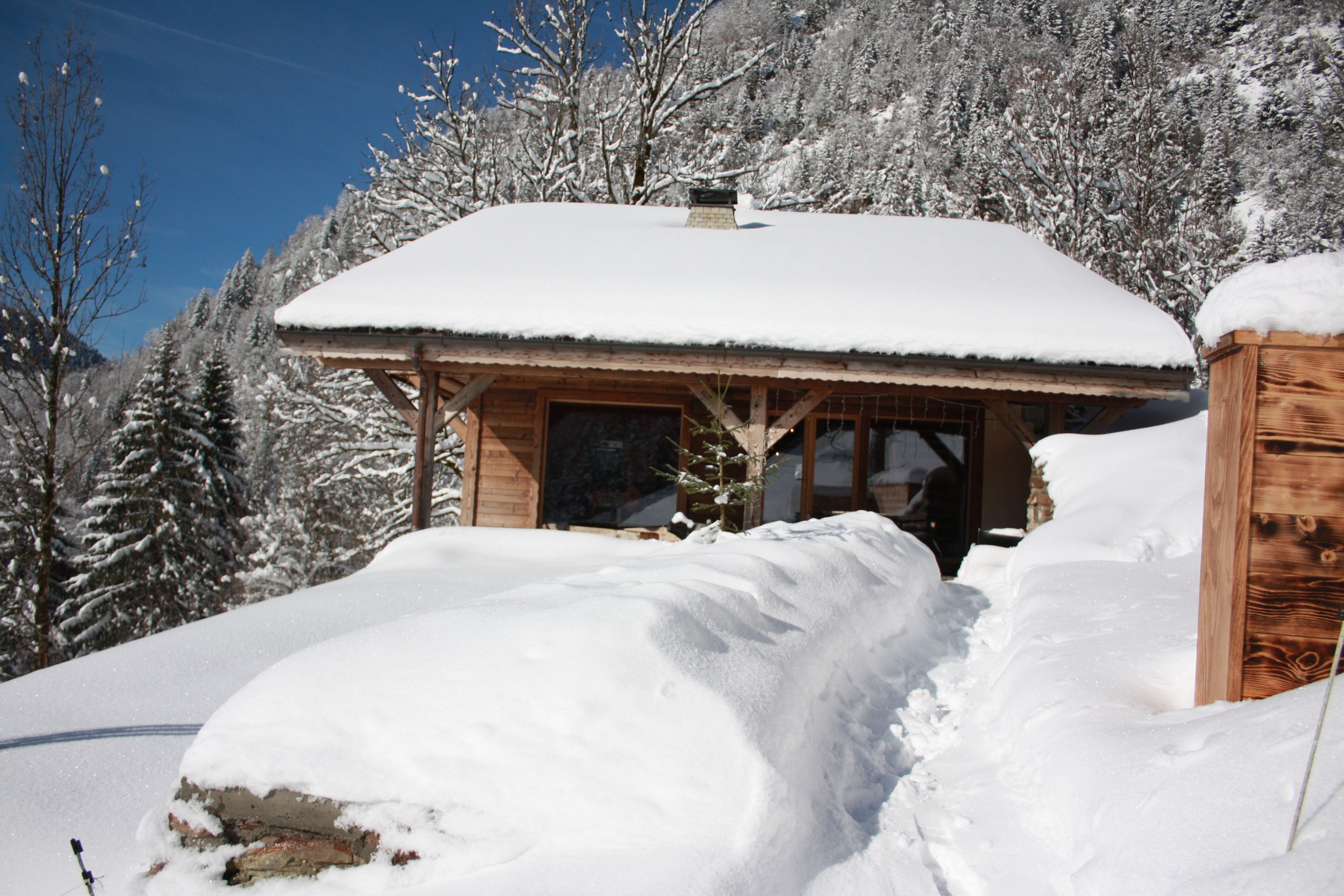 A wooden cabin with a snow-covered roof, surrounded by snow-laden trees.