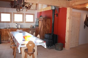A rustic kitchen with a long wooden table, chairs, a stove, and a red wall.