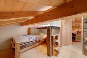 Un lit superposé en bois, avec une couvre-lit à motifs et une petite table en bois placée à côté.