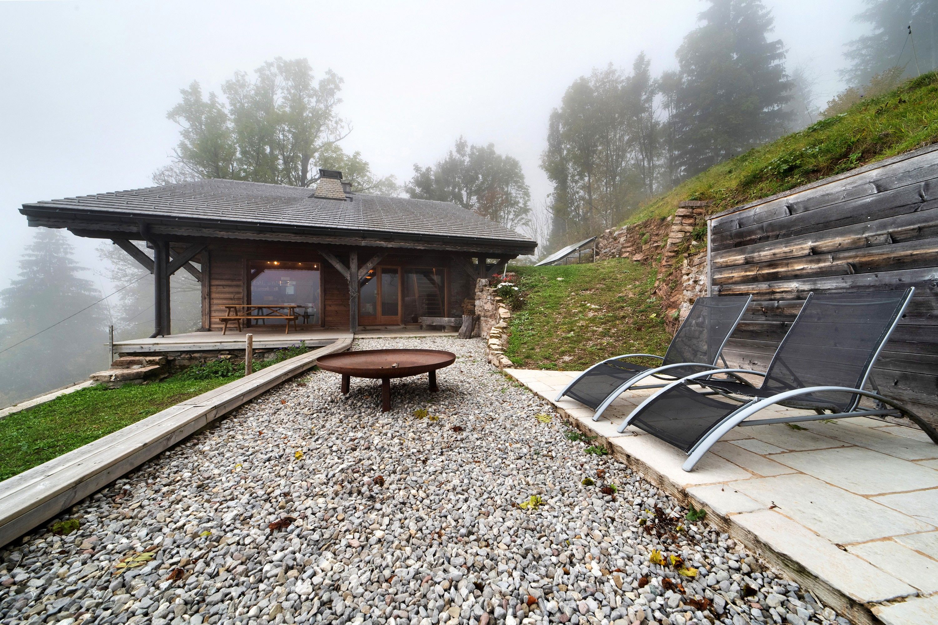 Un chalet rustique en bois doté d’un patio couvert, d’un chemin de gravier et d’un espace détente avec des chaises.
