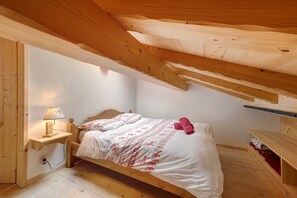 A bedroom with a wooden ceiling, a bed with patterned bedding, a bedside lamp, and a small wooden nightstand.