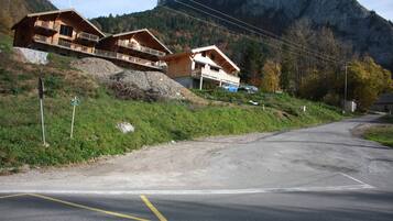Una cabana de muntanya amb diversos edificis de fusta, un camí de terra i una carretera amb una fletxa groga que indica un gir.