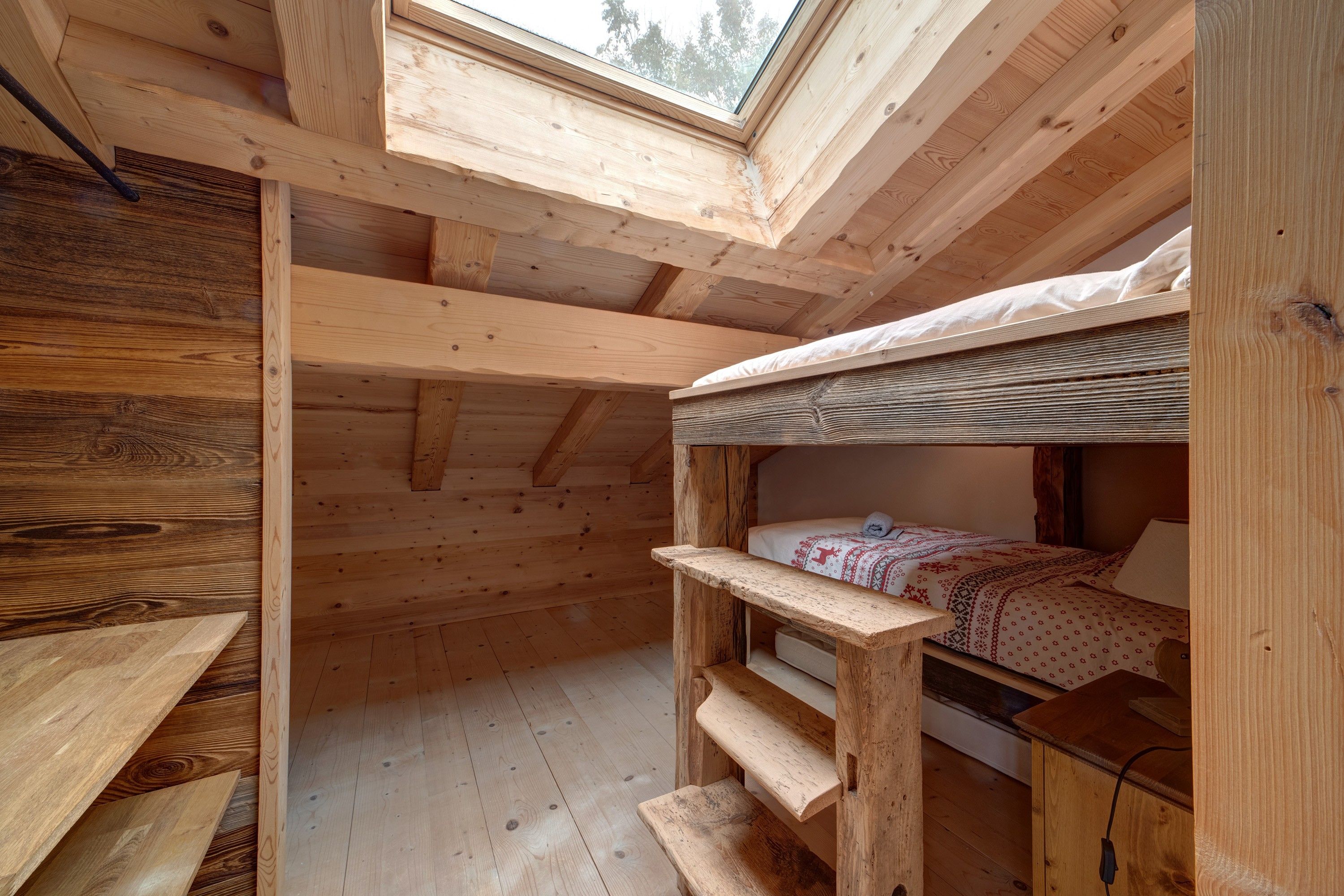 A wooden cabin interior with a skylight, bunk beds, and a wooden table.