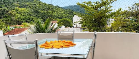An outdoor dining area with a glass table and metal chairs, overlooking a mountainous landscape.