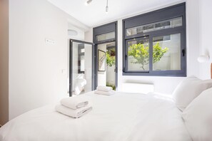 A modern bedroom with a large bed, white linens, and a view of a tree through a window. - FiftySeven Athens - Lemon Garden Hideaway | B3 (Athina)