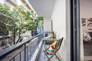 A balcony with a table, chairs, and a view of a tree-lined street. - FiftySeven Athens - Pedestrian St Balcony | 001 (Athina)