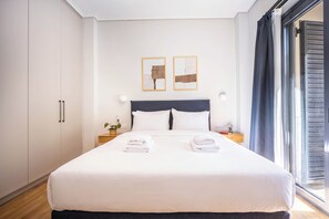 Hotellihuone, jossa on suuri sänky, kaksi yöpöytää, yölamppu, ruukkukasvi ja ikkuna, jossa on verhot.