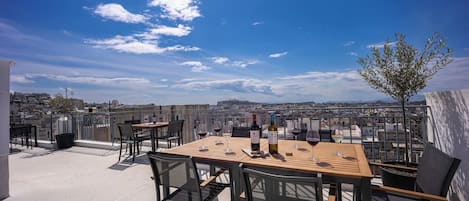 A rooftop terrace with a table set for dining, a view of the cityscape, and a clear sky.