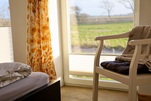 Ein Zimmer mit einem Bett, einem Sessel und einem Fenster mit Blick auf ein Feld.