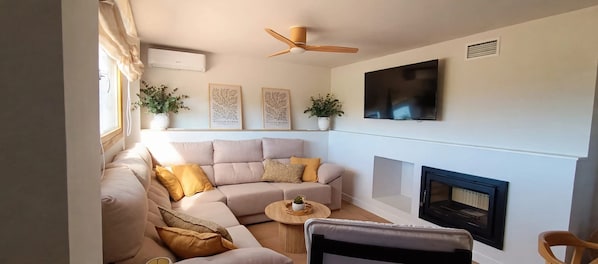 A living room with a beige sectional sofa, a round coffee table, a fireplace, and a ceiling fan.