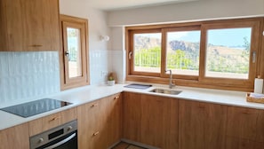 A kitchen with wooden cabinets, a white countertop, a built-in oven, a sink, and a window with a view of greenery and mountains.