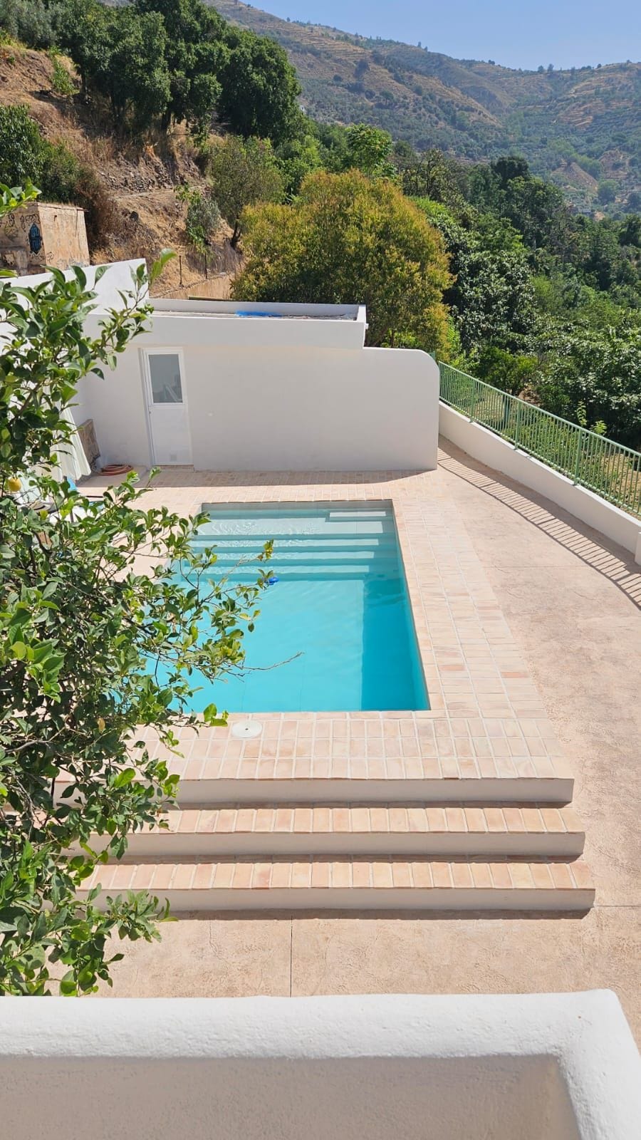 Una piscina rectangular con superficie de agua azul cristalina, rodeada por una solana con baldosas y una pared blanca.
