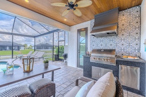 An outdoor patio with a grill, seating, and a view of a house. - Hot tub and pool, garage the best games, sleeps up to 8! (Cape Coral)
