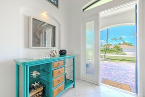 A teal console table with drawers, a mirror above it, and a view of a residential area through a glass door. - Hot tub and pool, garage the best games, sleeps up to 8! (Cape Coral)