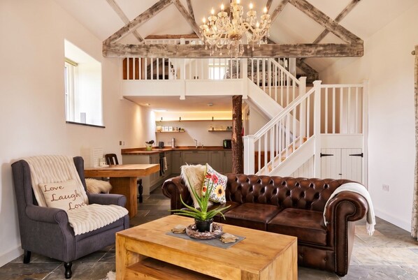 A spacious living room with a high ceiling, a fireplace, a dining area, and a staircase leading to an upper level.