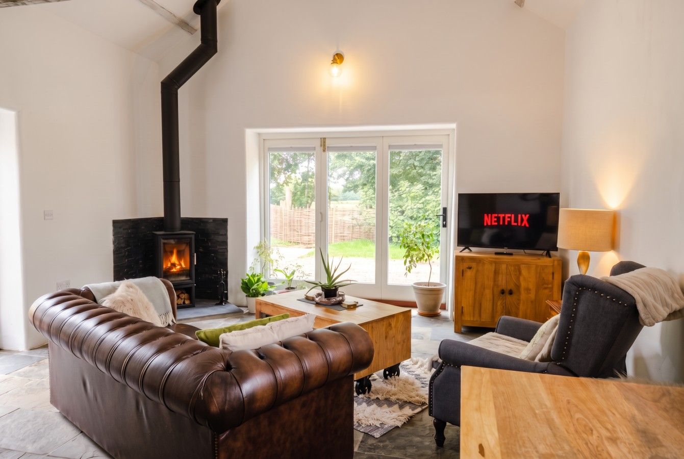 A living room with a fireplace, leather sofa, wooden coffee table, and a TV displaying 'NETFLIX'.