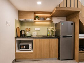 Cozinha compacta com micro-ondas embutido, geladeira de aço inoxidável, armários de madeira e bancada com diversos utensílios de cozinha.