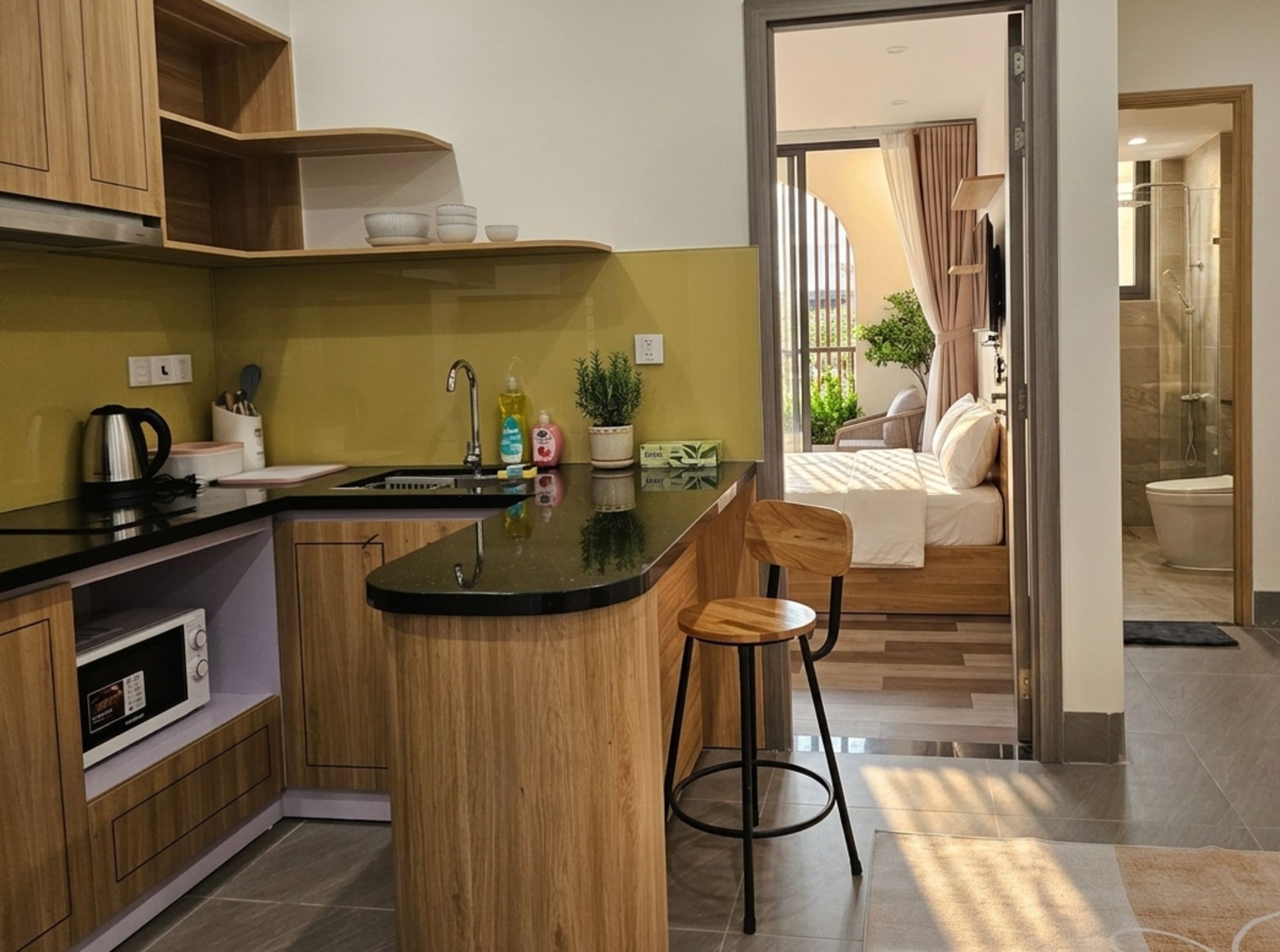 A modern kitchen with a central island, bar stools, and a view of a bedroom with a balcony.